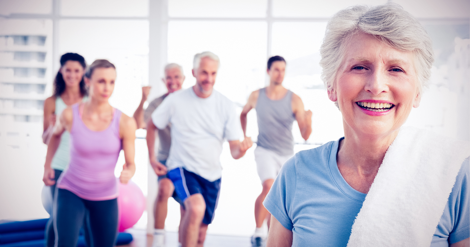 Portrait of a cheerful senior woman with people exercising in the background at fitness studio